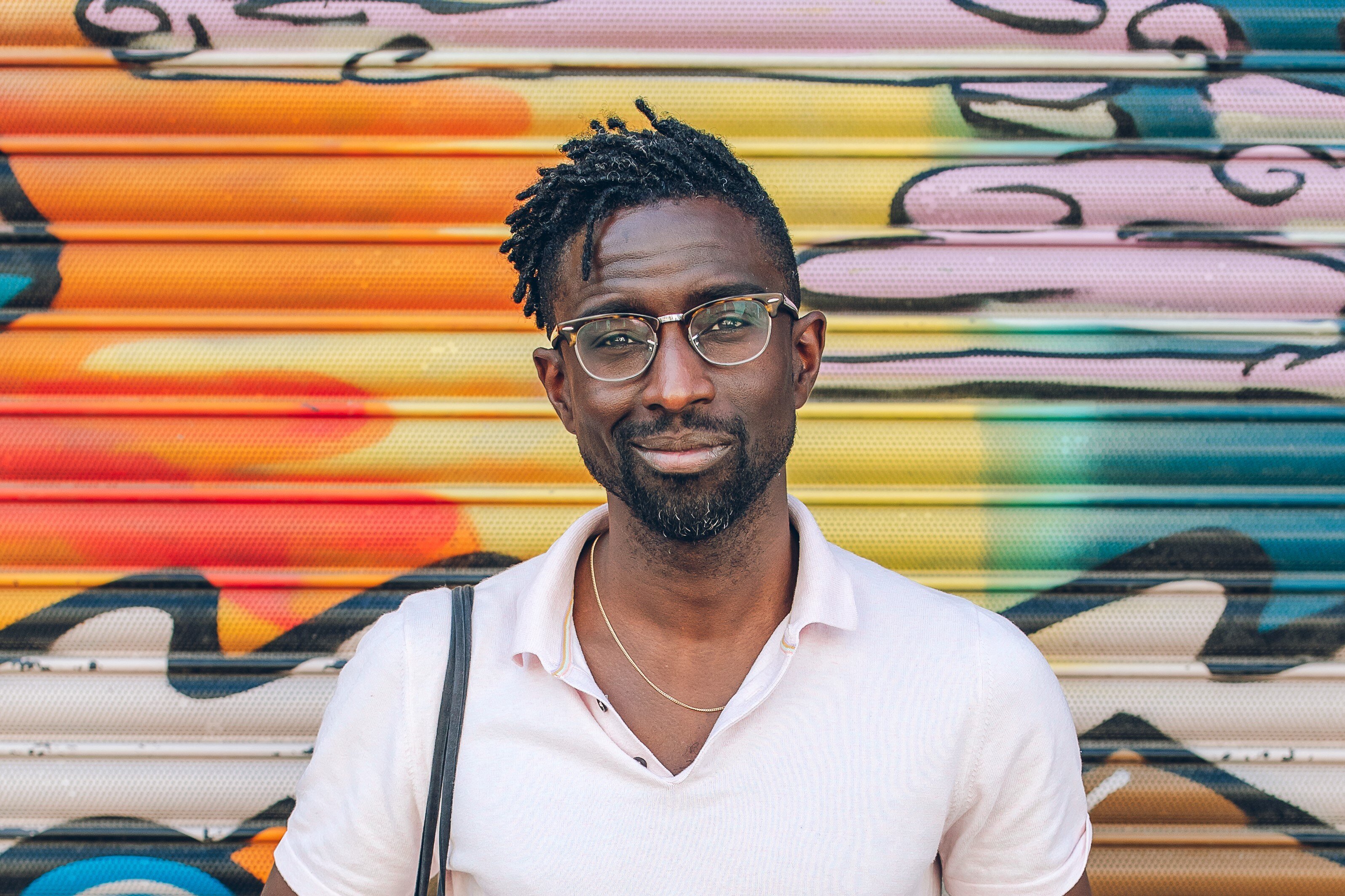 An image showing Jeffrey stood in front of a wall of graffiti art smiling at the camera